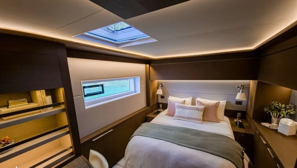 Master cabin aboard Aeolus catamaran with queen bed, grey throw blanket, art print and skylight hatch