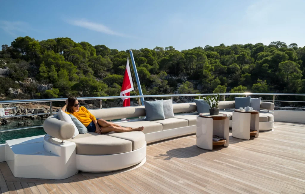 Guest relaxing on the sun deck lounge of O'Ptasia yacht with Mediterranean coastline view